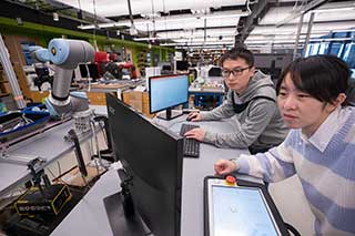 Two Khoury students look at a computer display while they work on a project