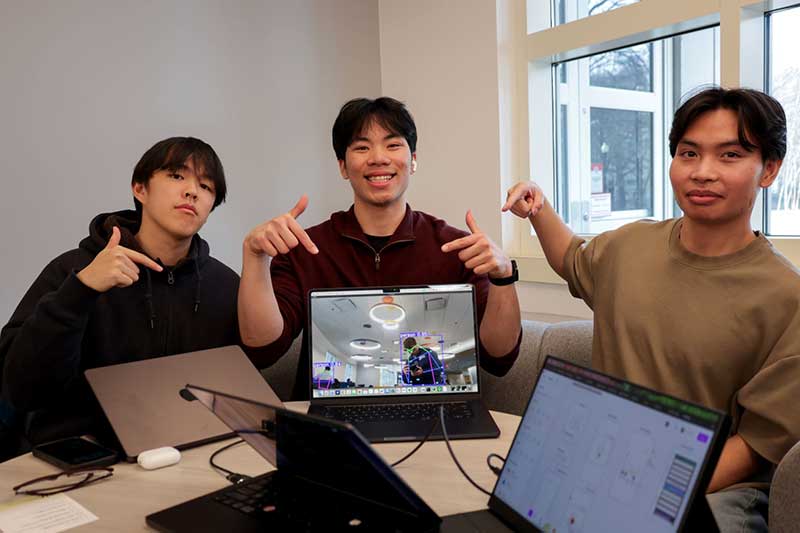 From left to right: Michael Zhang, Phillips Le, and Nghia Trang point at a laptop screen showing a video of their project
