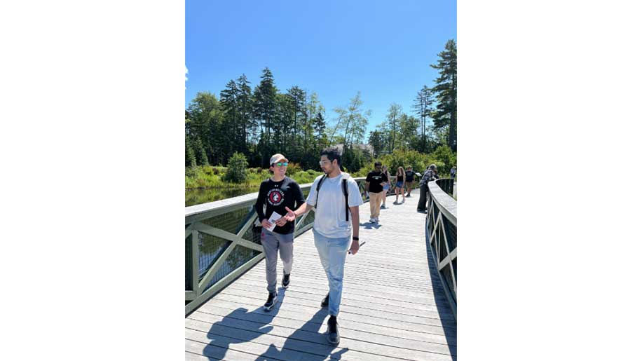 A group of Roux students walk across a footbridge at a botanical garden